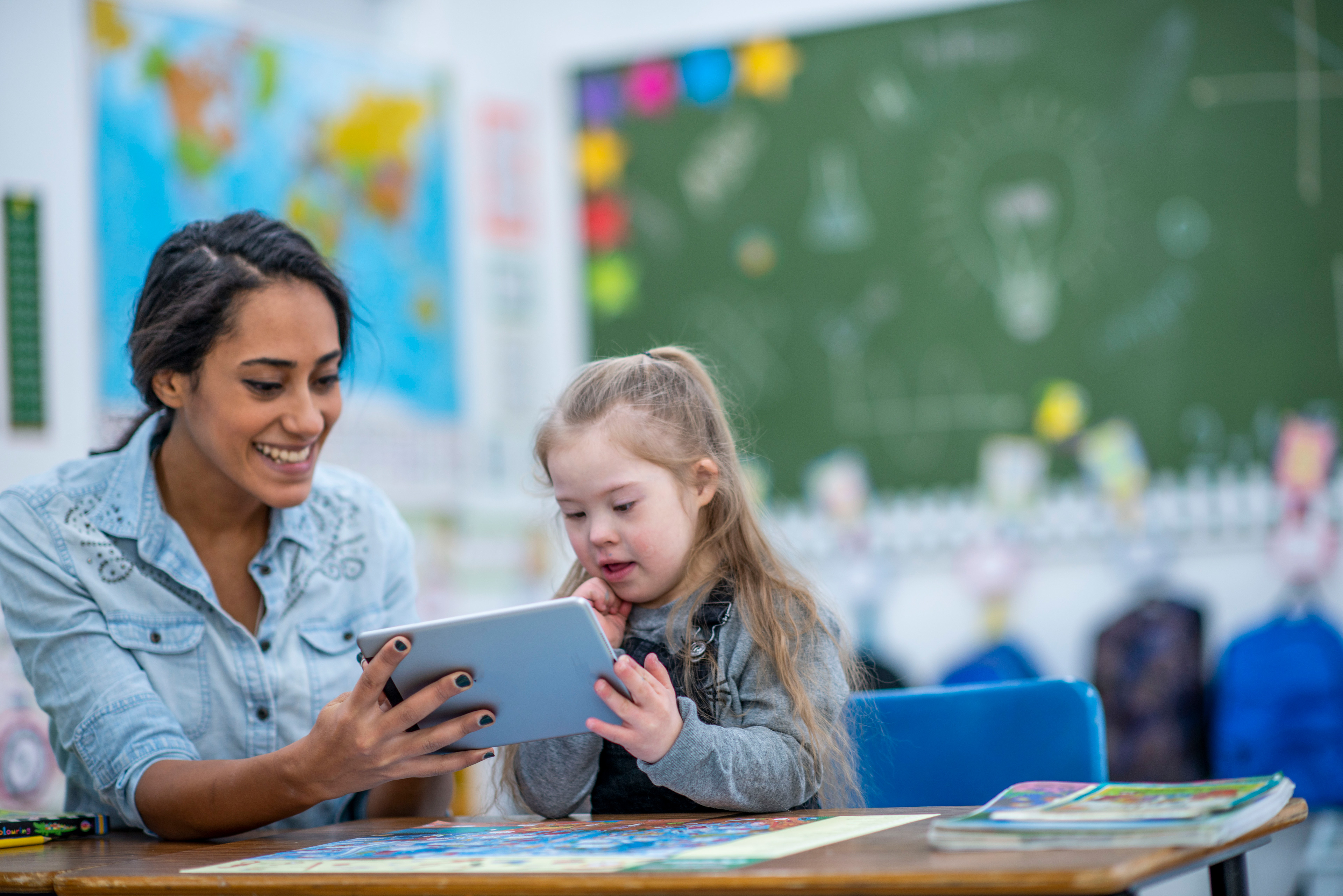 Eine Lehrerin schaut gemeinsam mit einem Mädchen mit Behinderung im Klassenzimmer auf ein Tablet.