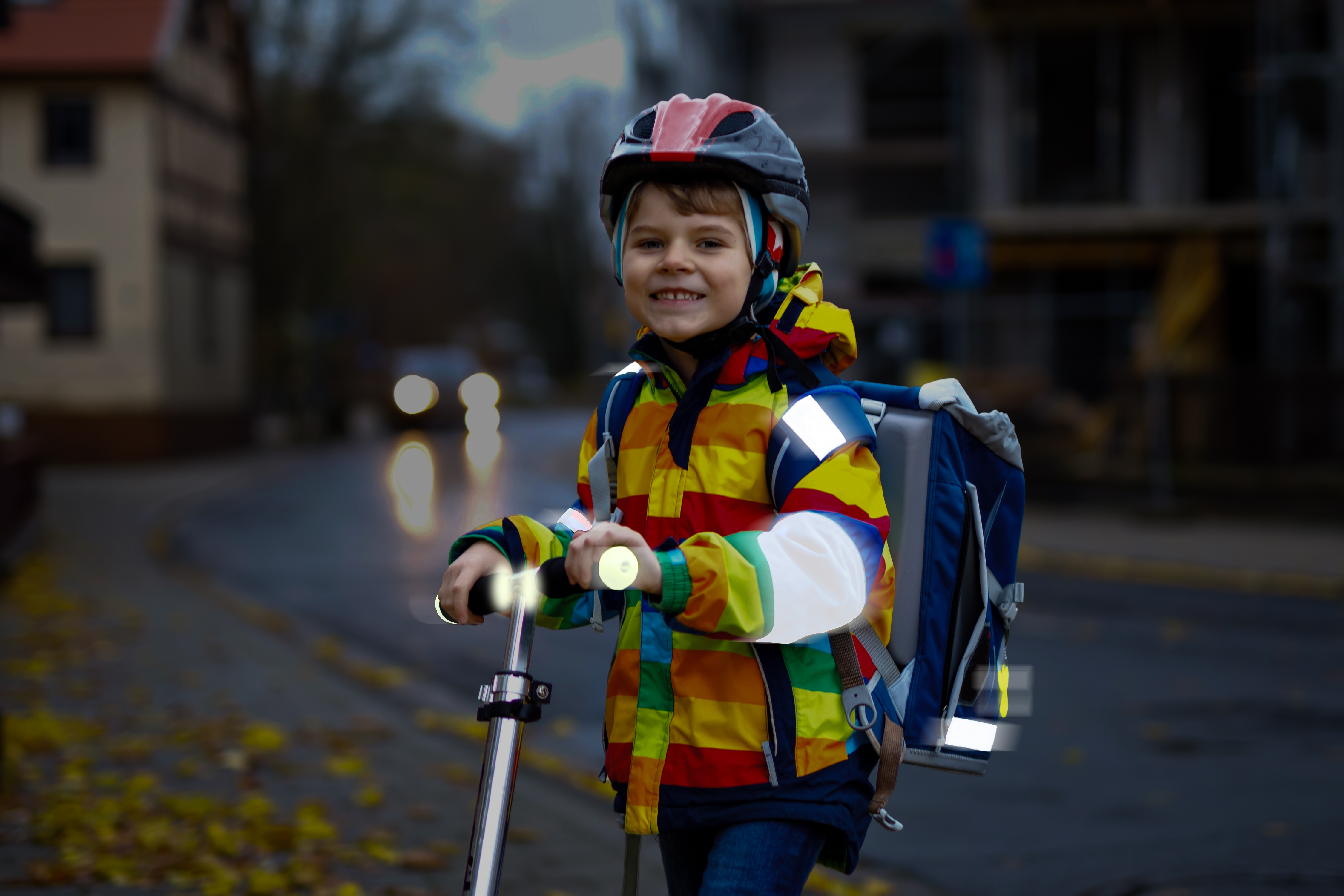 Ein Junge auf einem Tretroller wird in der Dämmerung angeleuchtet und seine Reflektoren leuchten auf.