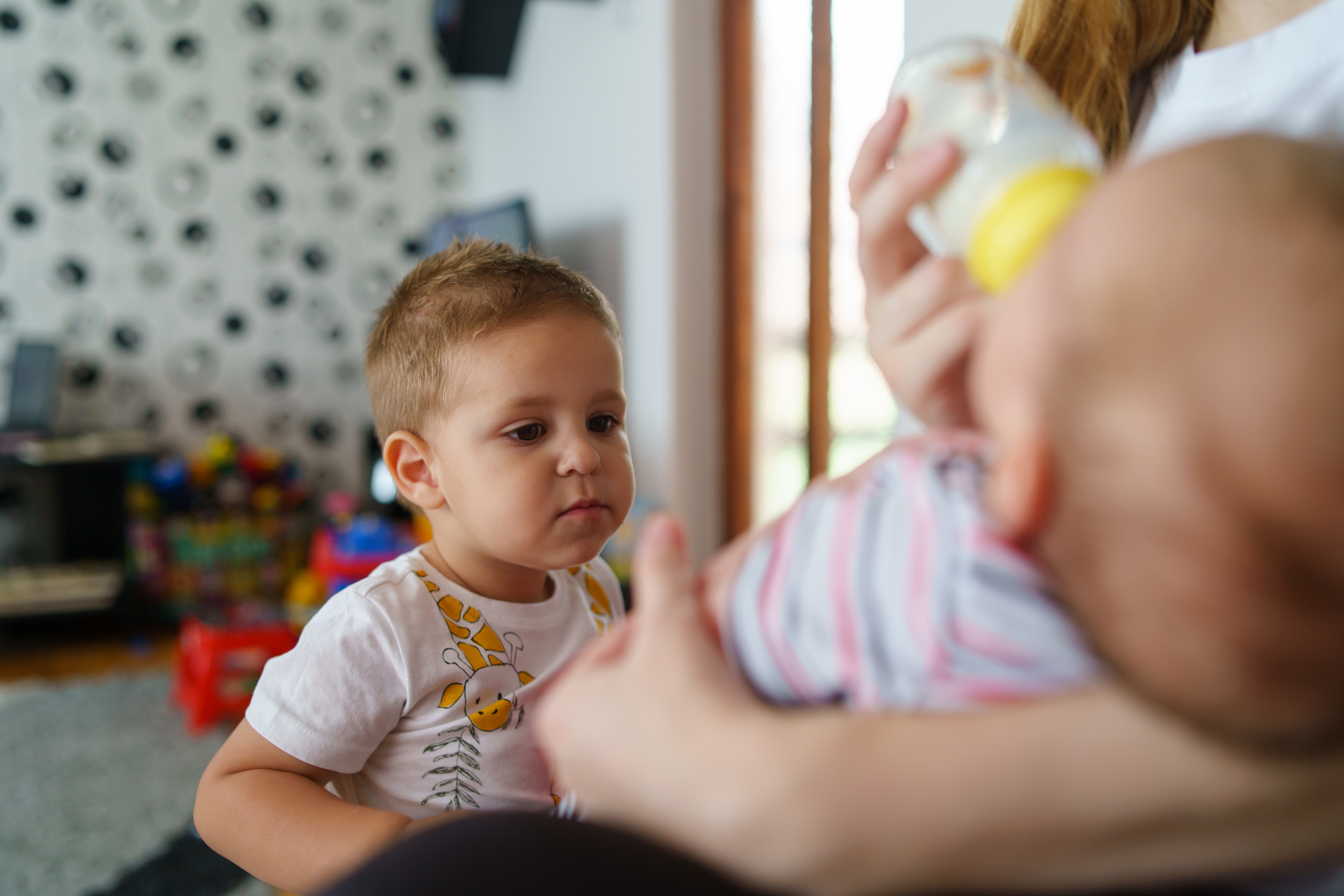 Eine Mutter gibt dem Baby die Flasche, das ältere Kind sieht zu.