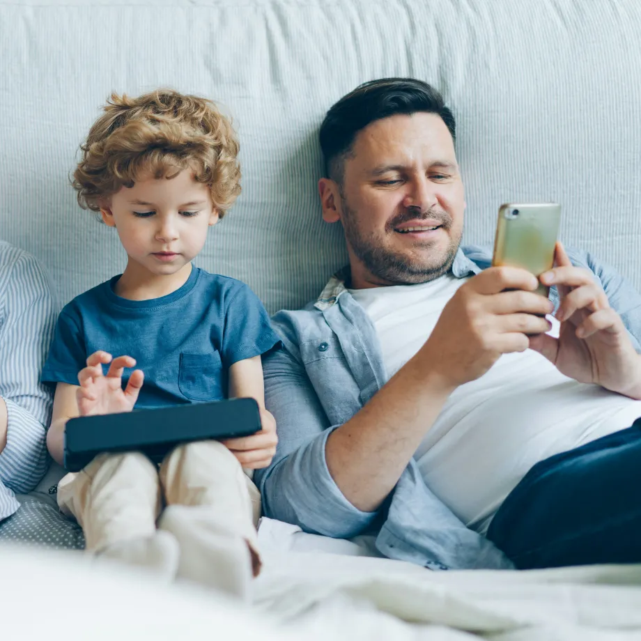 Vater liegt mit seinen zwei Söhnen im Bett und alle schauen aufs Handy