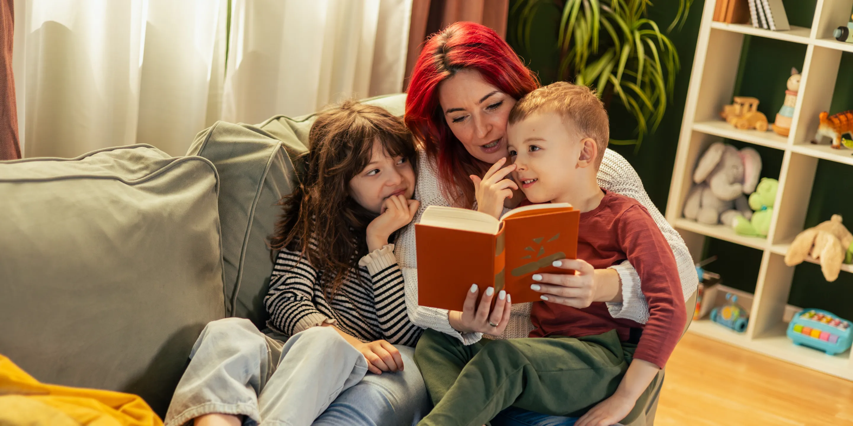 Eine Mutter liest zwei Kindern auf dem Sofa vor.
