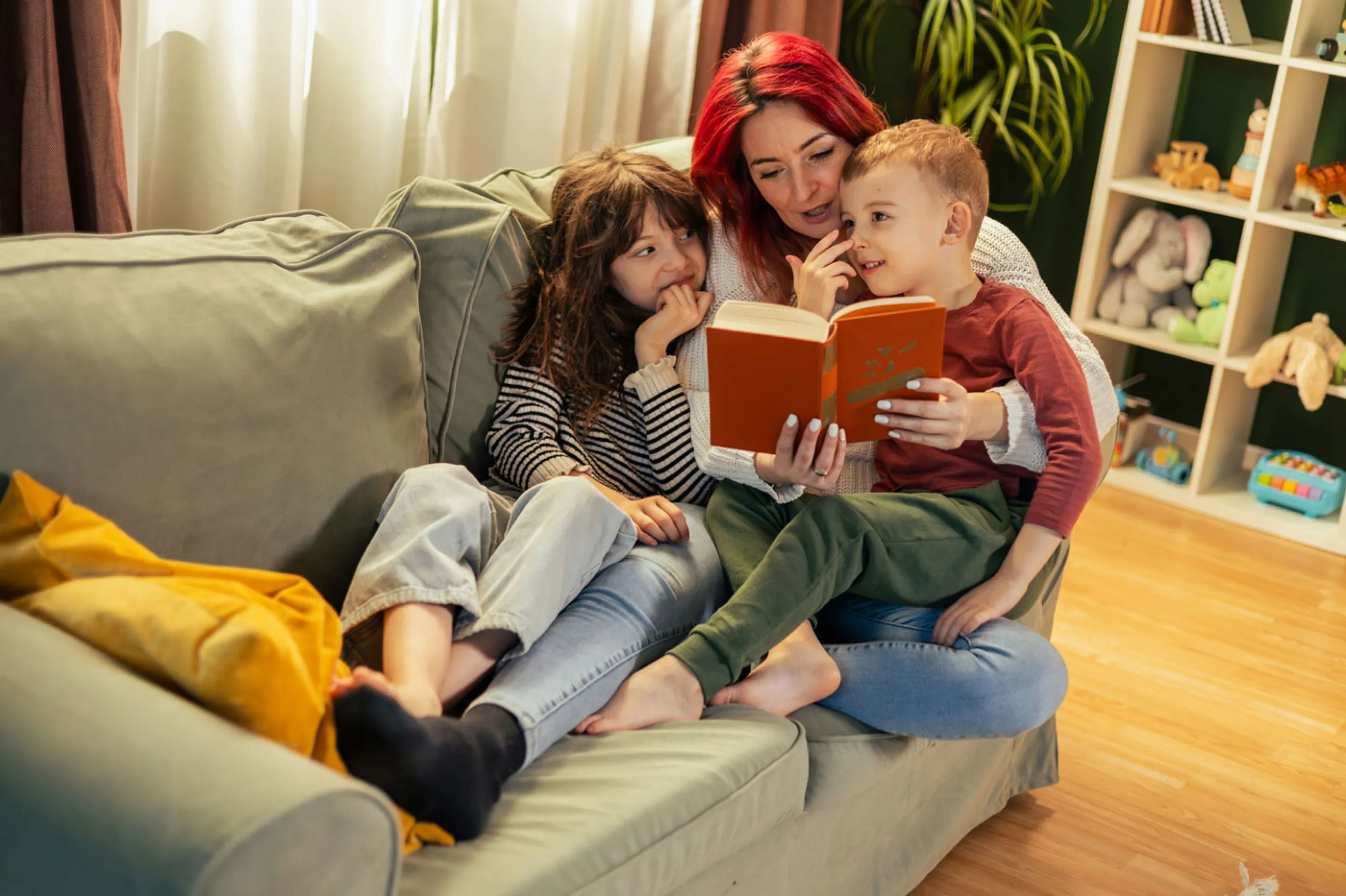 Eine Mutter liest zwei Kindern auf dem Sofa vor.