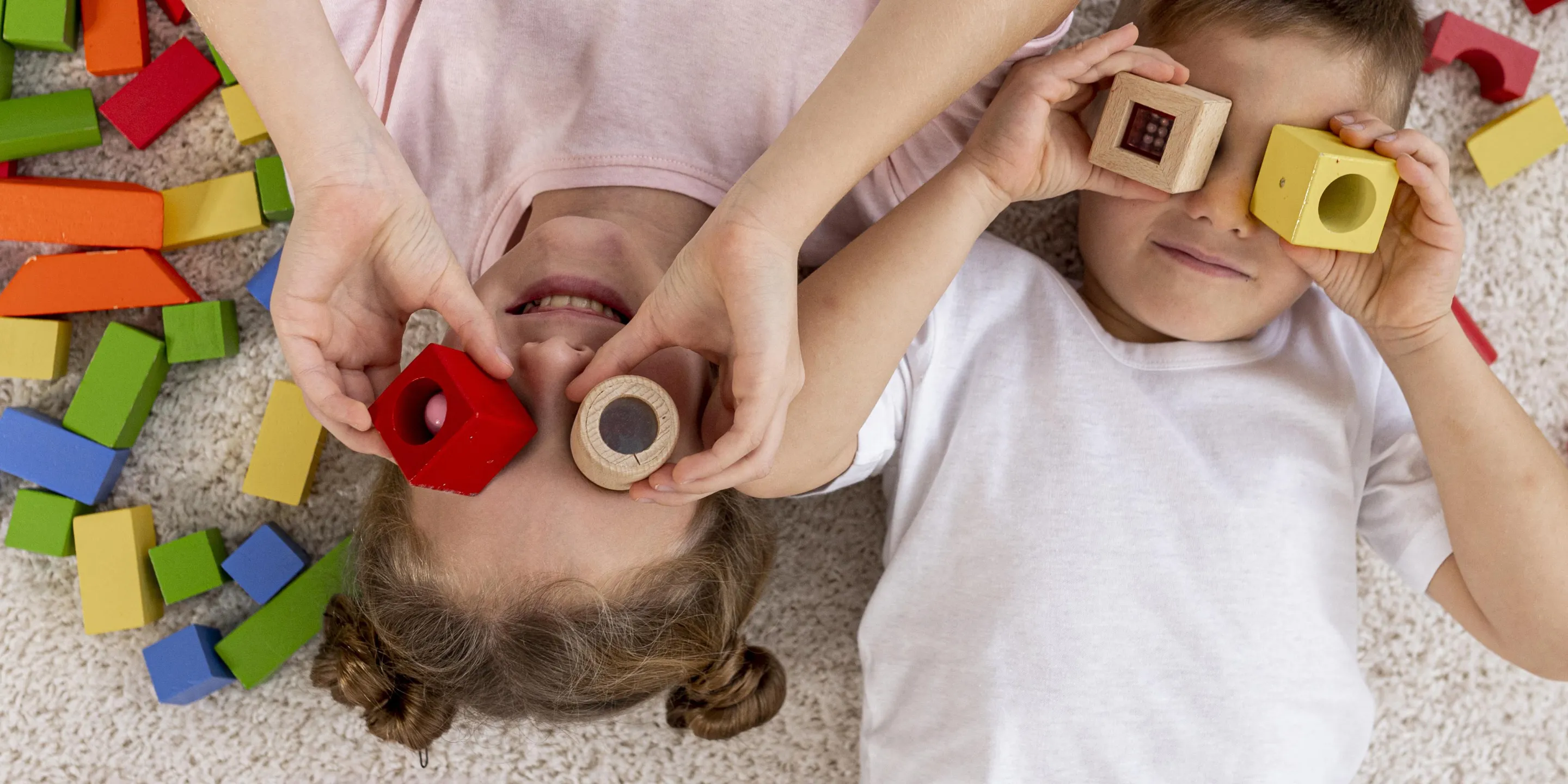 Zwei Kinder spielen mit Bauklötzen, die sie sich über die Augen halten wie Ferngläser.