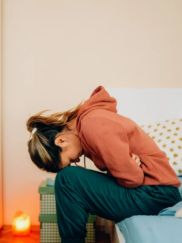 Jugendliche sitzt gekrümmt auf Bettkante