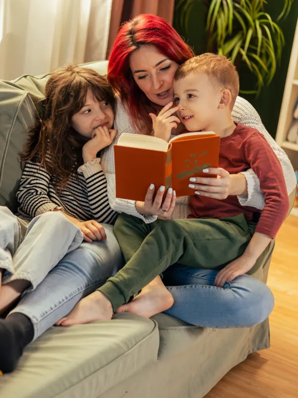 Eine Mutter liest zwei Kindern auf dem Sofa vor.