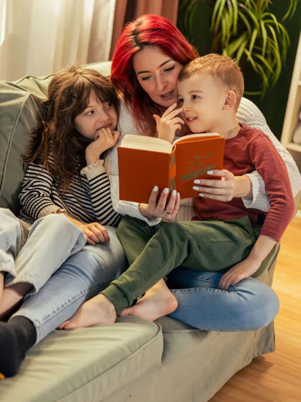 Eine Mutter liest zwei Kindern auf dem Sofa vor.