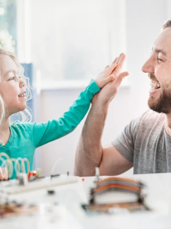 Ein Kindergartenkind und ein Vater geben sich ein High-Five.
