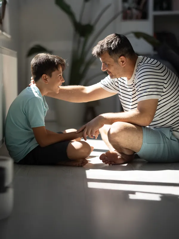 Ein Vater führt auf dem Boden sitzend ein ruhiges, klärendes Gespräch mit seinem Sohn.