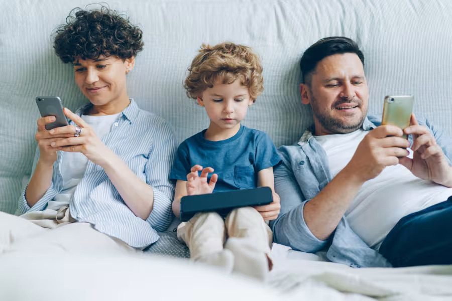 Vater liegt mit seinen zwei Söhnen im Bett und alle schauen aufs Handy