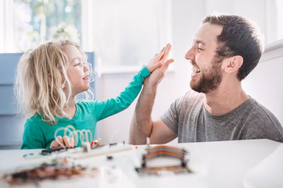 Ein Kindergartenkind und ein Vater geben sich ein High-Five.