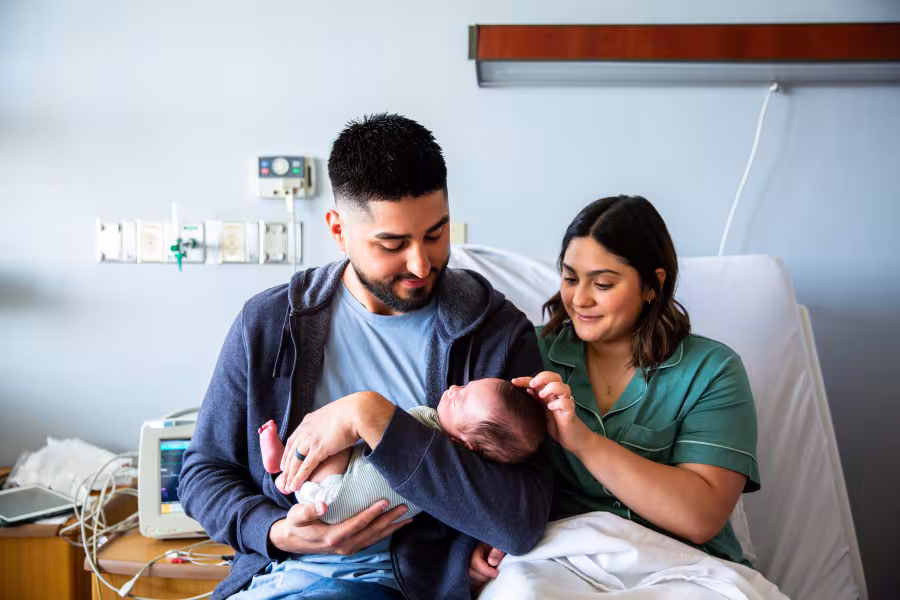Vater, Mutter und Baby sitzen nach der Geburt glücklich zusammen im Krankenhausbett.