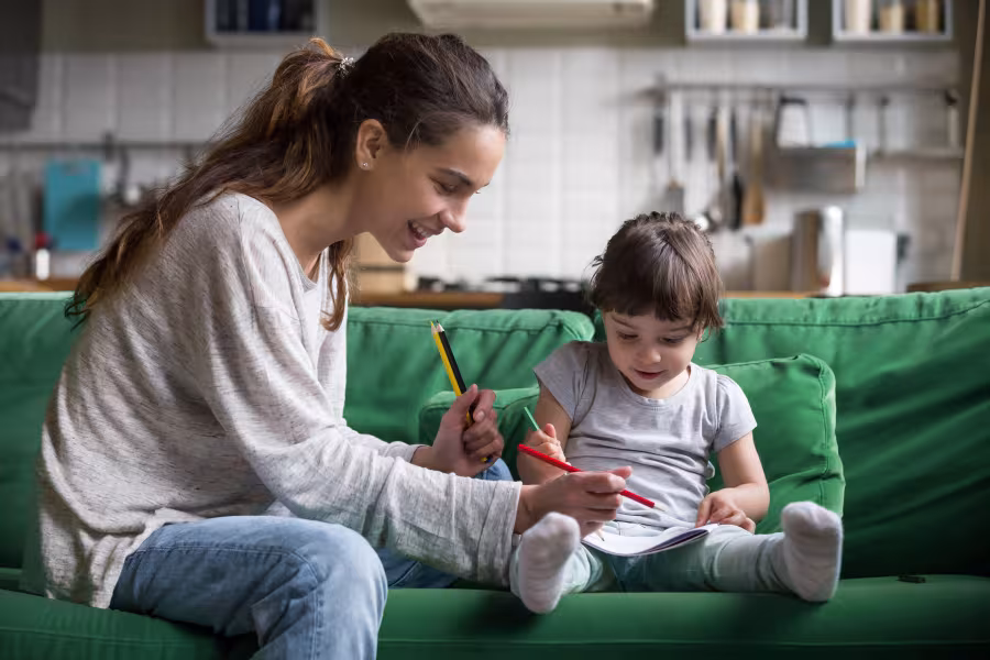 Eine Babysitterin malt etwas mit einem jungen Mädchen.