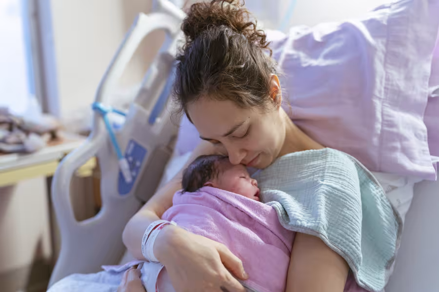 Eine Mutter kuschelt im Krankenhausbett mit ihrem Neugeborenen.