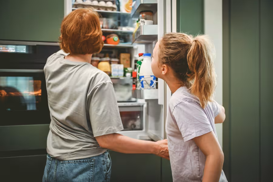 Mutter und Tochter blicken in den geöffneten Kühlschrank.