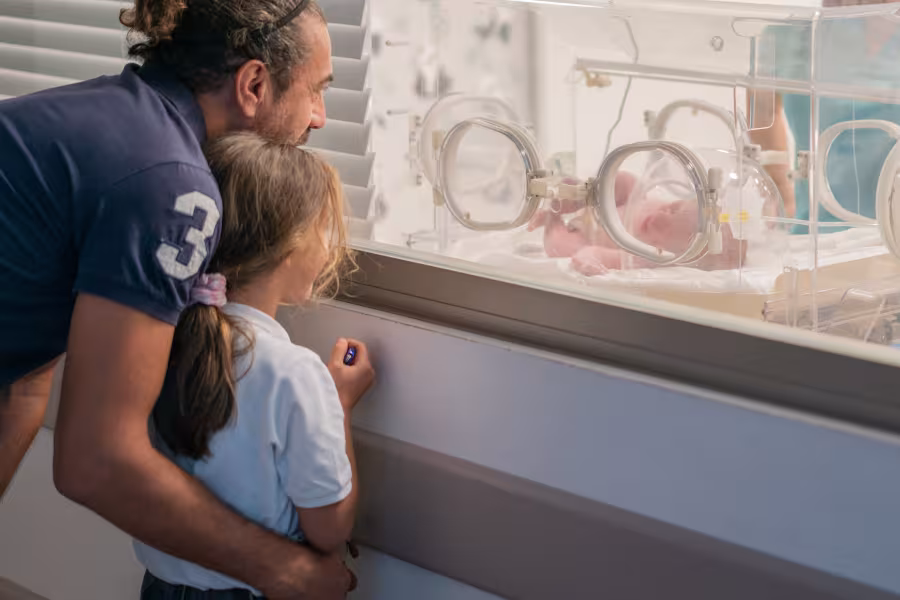 Ein Vater besucht mit seiner Tochter das frühgeborene Geschwisterchen auf der Neonatologie.